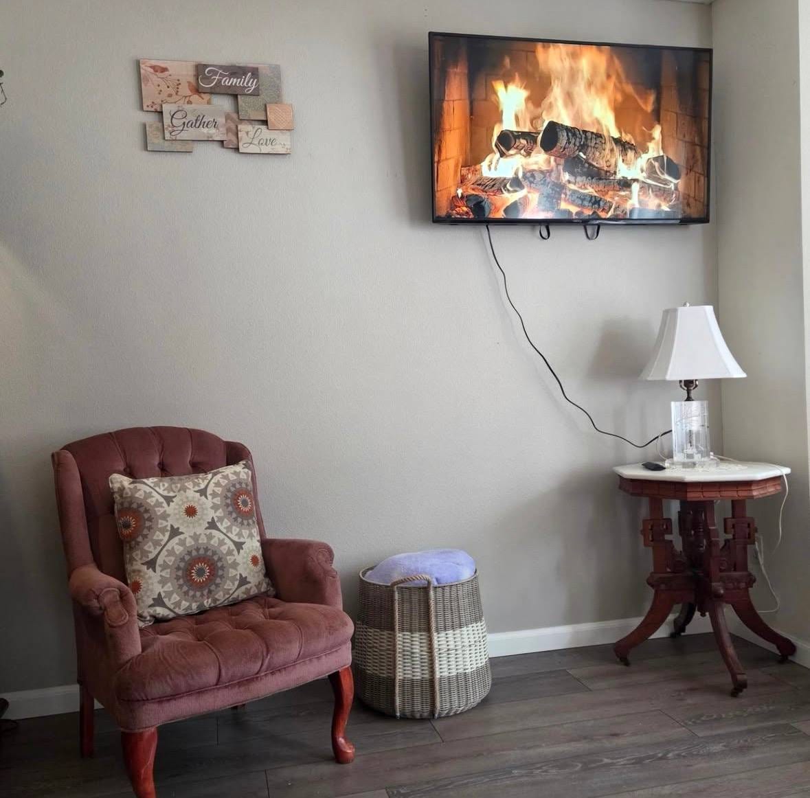 A cozy reading corner with a tufted armchair, fireplace, and Family Gather Love sign.