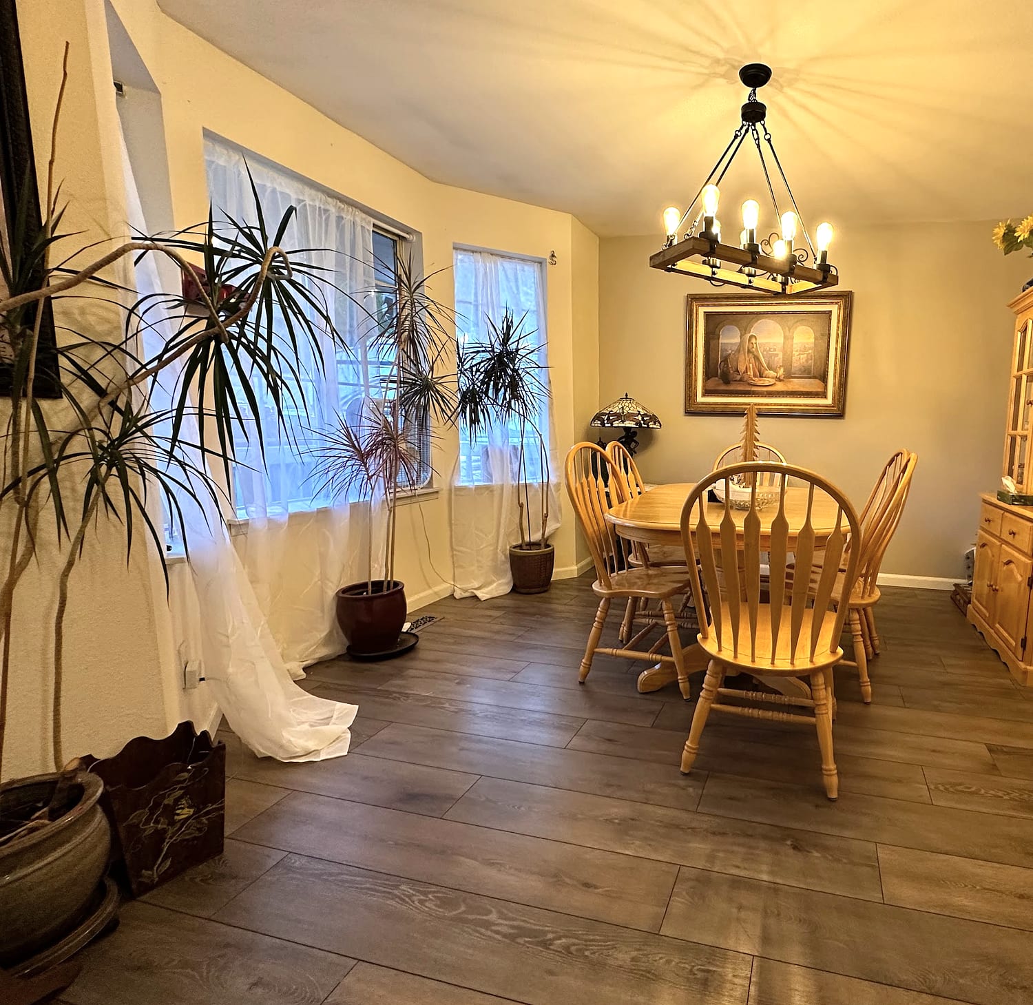 The JOY-Graham dining room with a wood table, chandelier, and plants by the windows.