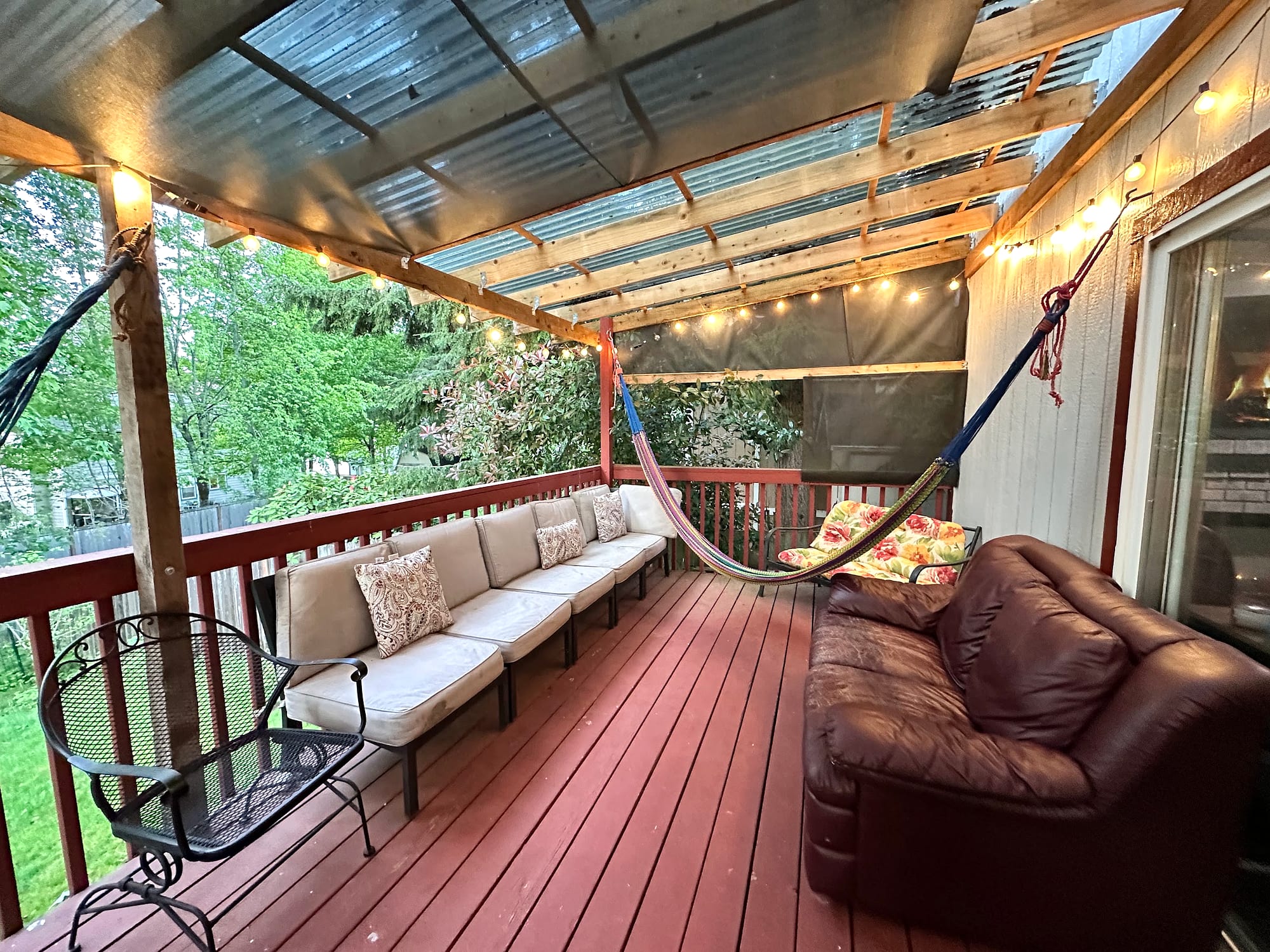 The covered back deck at JOY-Graham — warm string lights, cushioned seating, and a garden view.