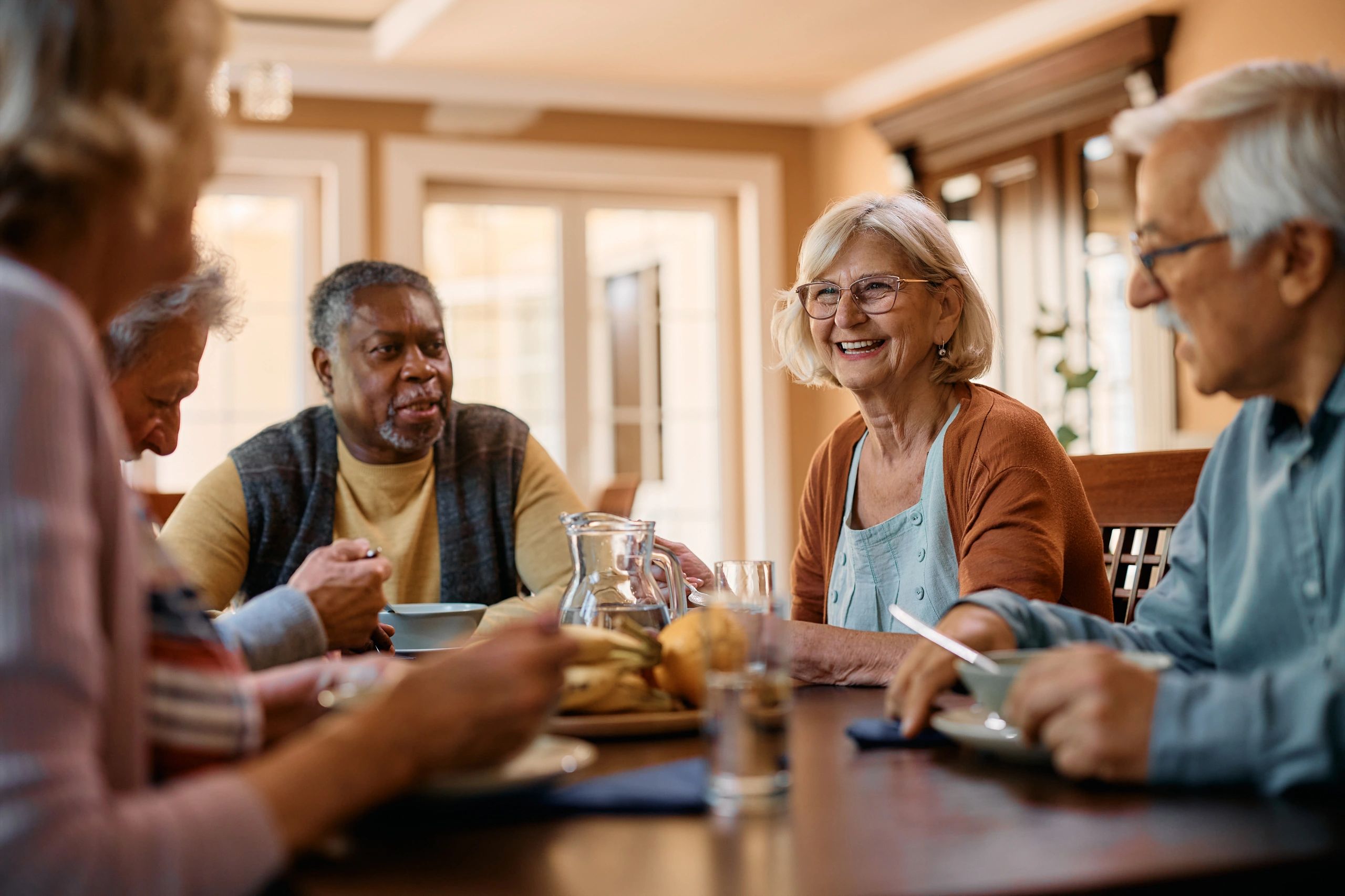 Older friends sharing a meal and laughing together at the table.