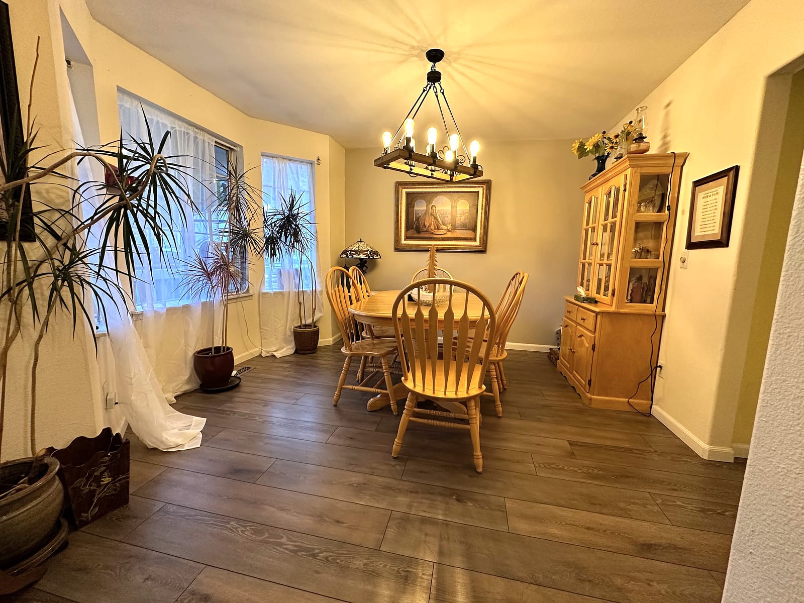 Warm dining room with a wood table, chandelier, and plants.
